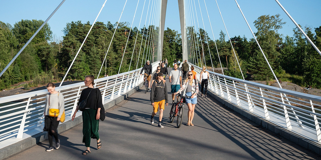 Several people are walking along a pedestrian bridge on a sunny day.