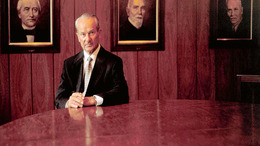 The founder Reinhard Mohn sitting in front of portraits of his ancestors.