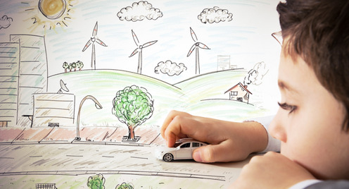 Ein Junge spielt mit einem Spielzeugauto. Im Hintergrund ist ein gemaltes Bild einer Stadt mit Windkraftanlagen und Sonnenenergiekollektoren.